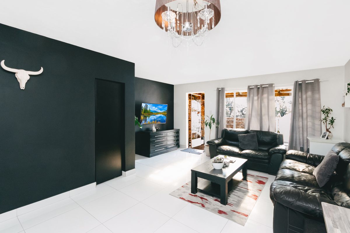 A bright living room featuring high-contrast black accent walls, white tiled flooring, and large windows allowing for ample natural light.