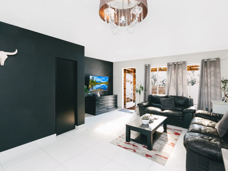 A bright living room featuring high-contrast black accent walls, white tiled flooring, and large windows allowing for ample natural light.