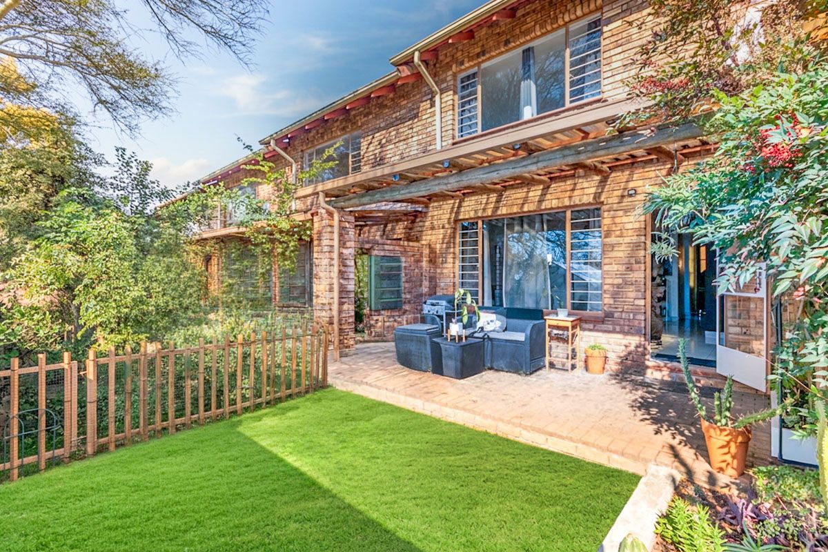 Rear view of the apartment featuring a brick facade, a timber pergola over a paved patio, and access to the interior through sliding glass doors.