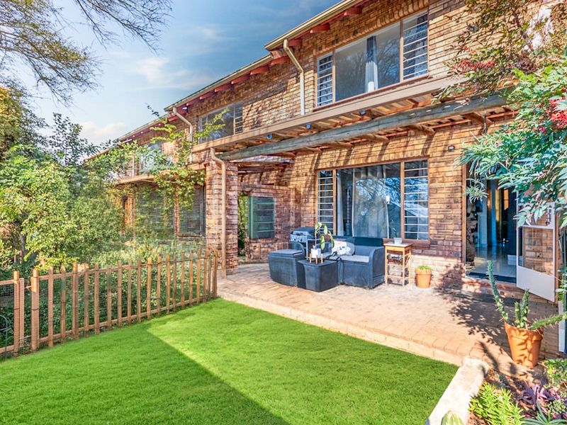Rear view of the apartment featuring a brick facade, a timber pergola over a paved patio, and access to the interior through sliding glass doors.