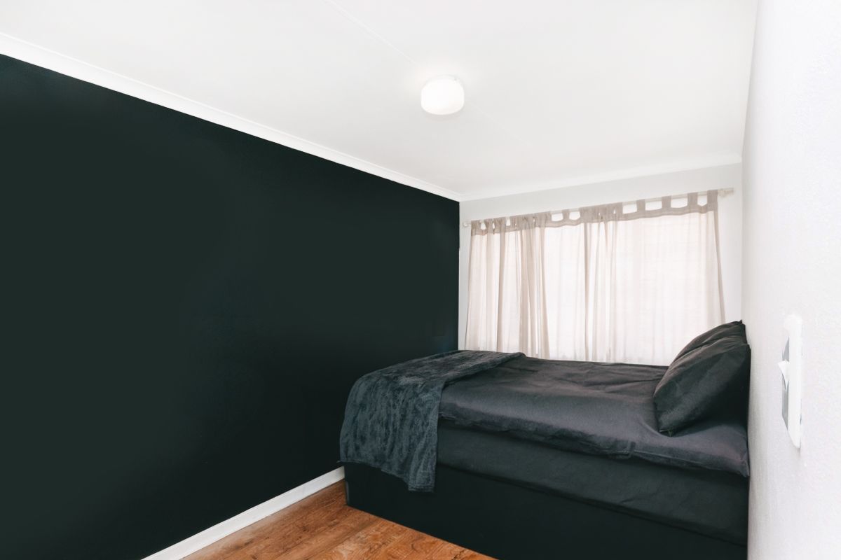 A bedroom featuring dark accent wall, laminate flooring, and a central ceiling light fixture.