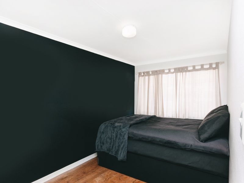 A bedroom featuring dark accent wall, laminate flooring, and a central ceiling light fixture.