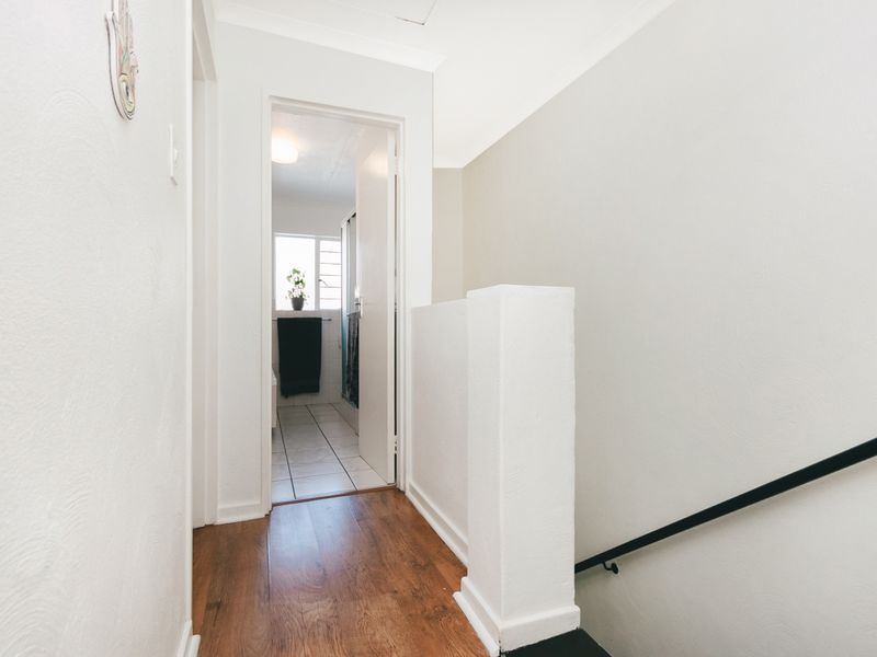 A bright, clean hallway featuring laminate flooring and a staircase with a black handrail, leading towards a bathroom area.