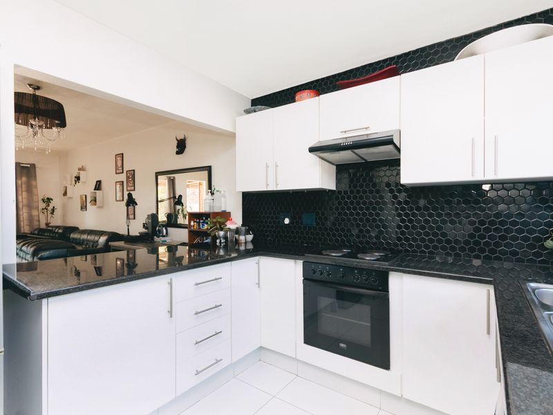Modern open-plan kitchen featuring white cabinetry, black granite countertops, and a striking black hexagonal tile backsplash, seamlessly flowing into the adjacent living area.
