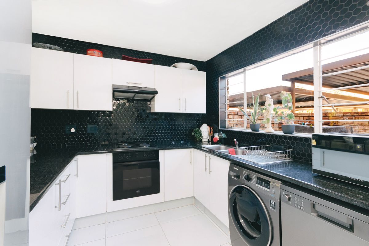 Modern kitchen featuring white cabinetry, contrasting black hexagonal tile backsplash, black granite countertops, and integrated oven with extractor fan.