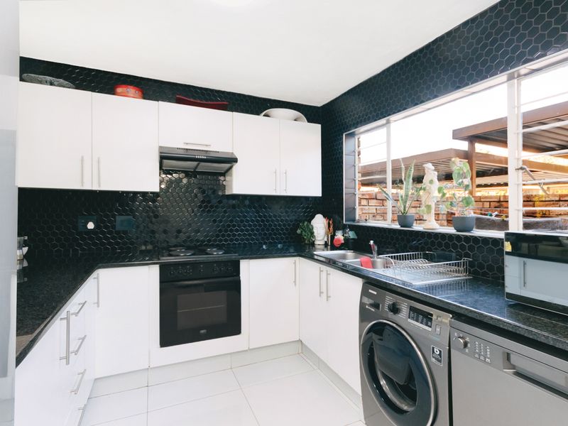 Modern kitchen featuring white cabinetry, contrasting black hexagonal tile backsplash, black granite countertops, and integrated oven with extractor fan.