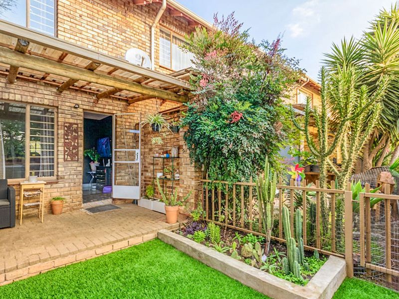 A private rear garden featuring a paved patio area with a timber pergola, raised garden beds, and a well-maintained artificial lawn.