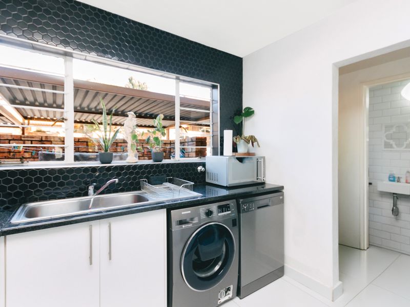 A functional scullery featuring a stainless steel sink, black granite countertops, and a modern hexagonal tile backsplash, with direct access to an adjacent bathroom.
