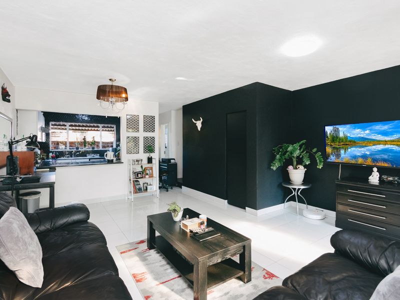 An open-plan living area featuring white tiled flooring, a modern kitchen with a breakfast bar, and a bold black accent wall.
