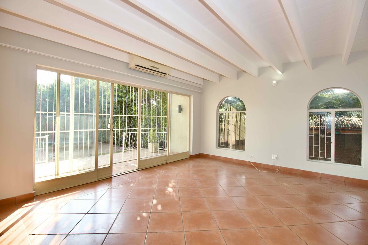 Spacious living area featuring terracotta floor tiles, exposed beam ceilings, and large sliding glass doors providing access to the outdoor patio.