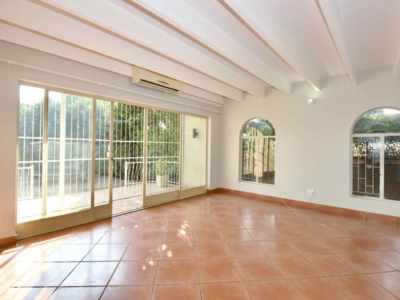 Spacious living area featuring terracotta floor tiles, exposed beam ceilings, and large sliding glass doors providing access to the outdoor patio.