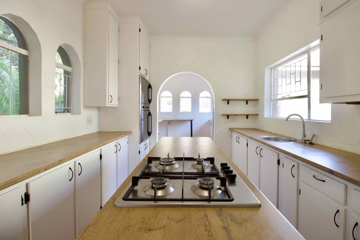 A bright, modern kitchen featuring white cabinetry, wooden countertops, a central gas hob, and distinctive arched architectural details.