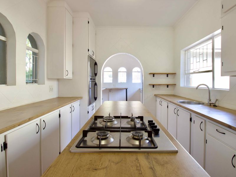 A bright, modern kitchen featuring white cabinetry, wooden countertops, a central gas hob, and distinctive arched architectural details.