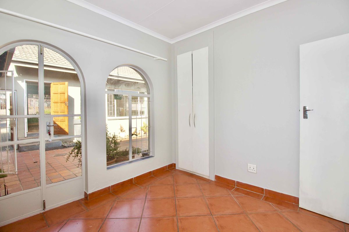 A bright, empty bedroom featuring terracotta floor tiles, built-in wardrobes, and arched windows providing natural light and access to the outdoor patio area.