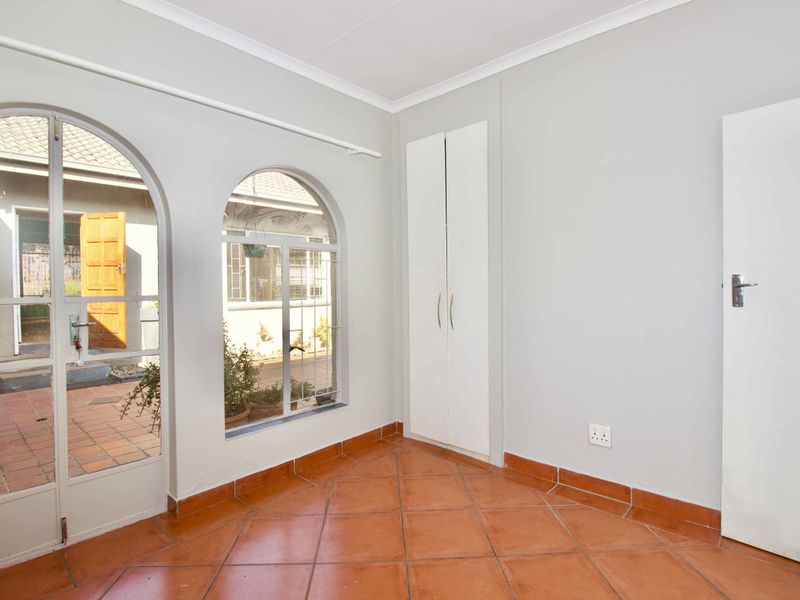 A bright, empty bedroom featuring terracotta floor tiles, built-in wardrobes, and arched windows providing natural light and access to the outdoor patio area.