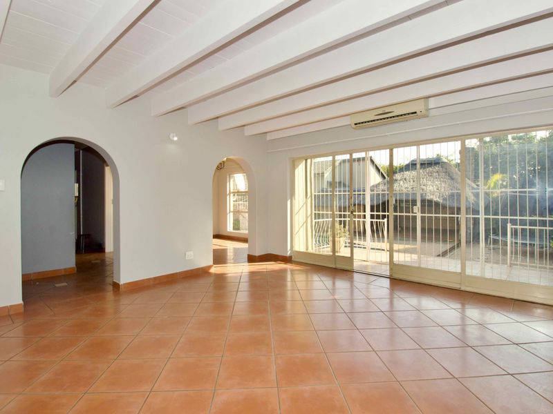 Spacious living area featuring terracotta floor tiles, exposed beam ceilings, and large sliding glass doors providing access to the outdoor area.