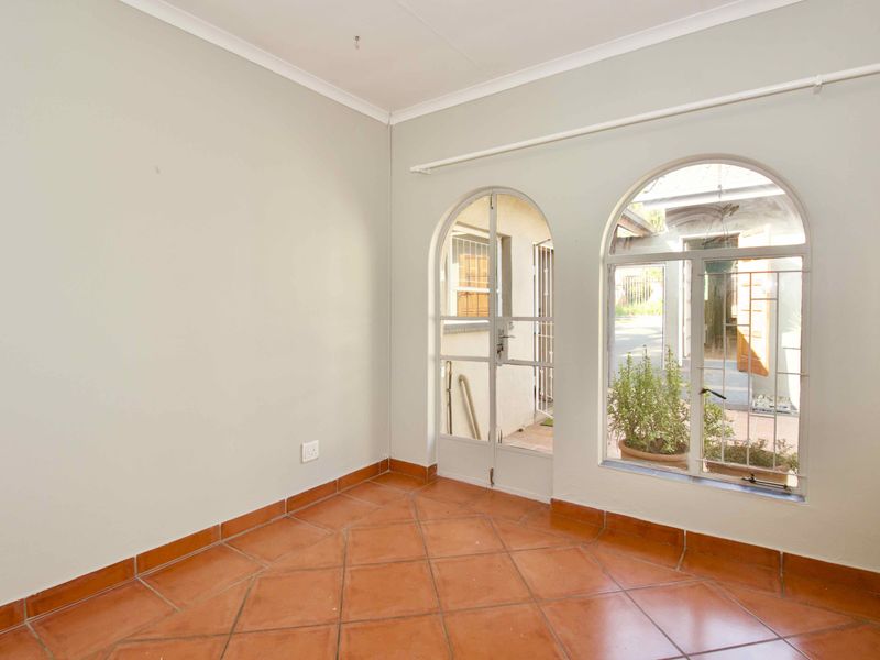 An empty living area featuring terracotta floor tiles, arched windows, and arched glass doors providing access to the exterior.