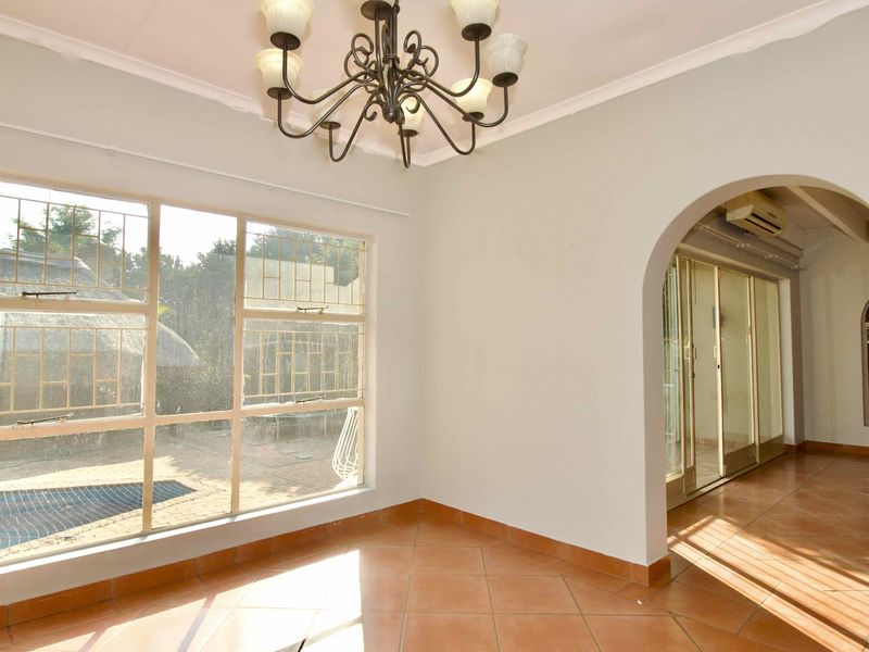 Bright and spacious living area featuring ceramic tile flooring, an elegant archway, and large windows with security bars, offering a view of the outdoor area.
