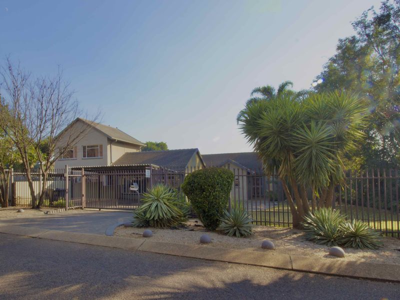 Front view of the property featuring a paved driveway, carport, and secure metal perimeter fencing with established garden landscaping.