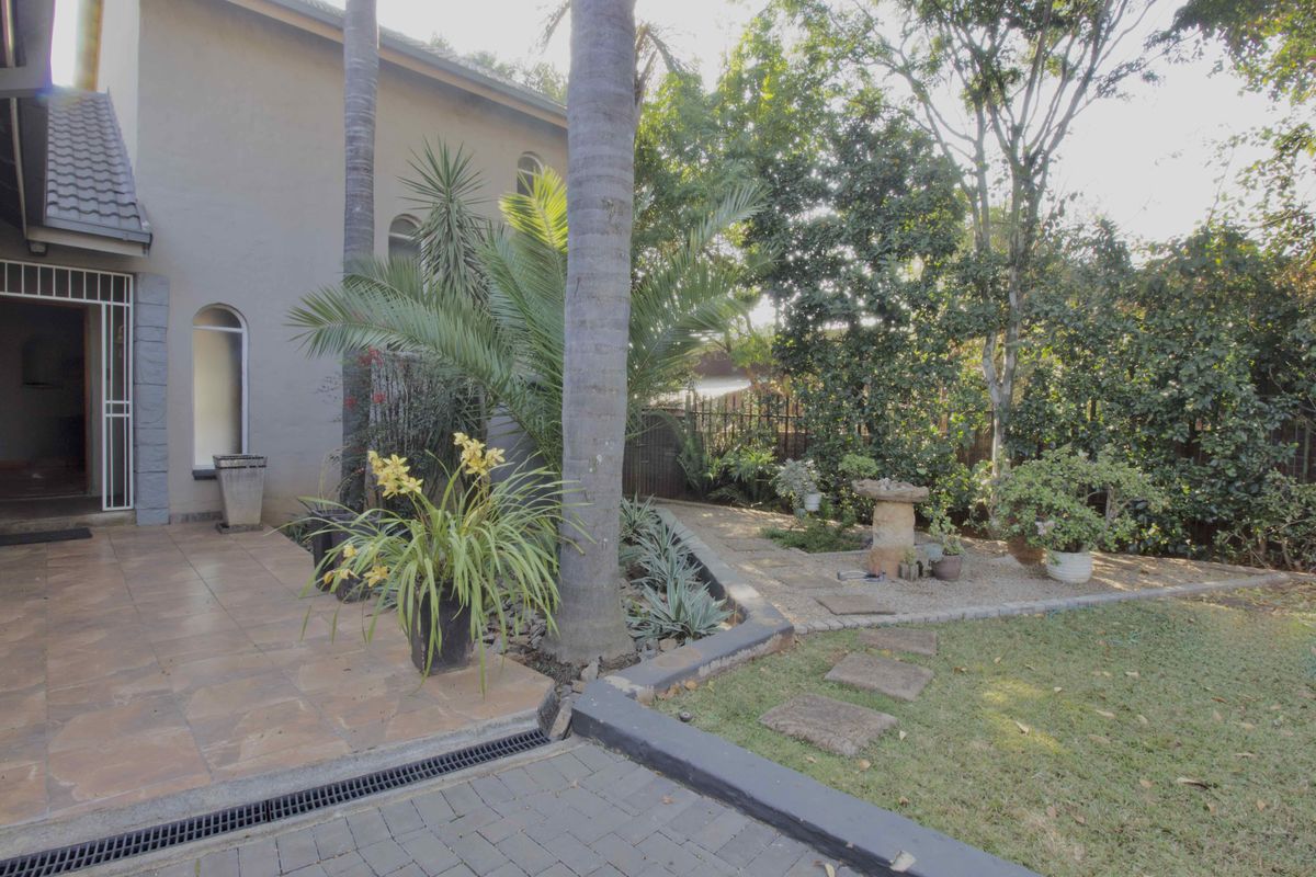 A well-maintained rear garden area featuring a tiled patio, paved driveway, and established landscaping with a retaining wall and drainage system.