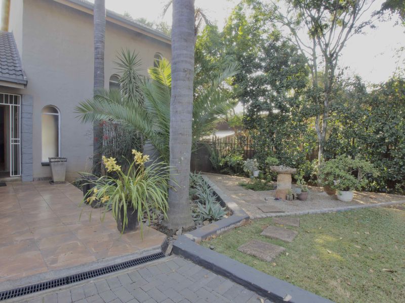A well-maintained rear garden area featuring a tiled patio, paved driveway, and established landscaping with a retaining wall and drainage system.