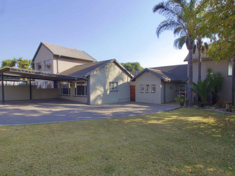 Front view of the property featuring a paved driveway, covered carport, and well-maintained exterior facade with arched window detailing.