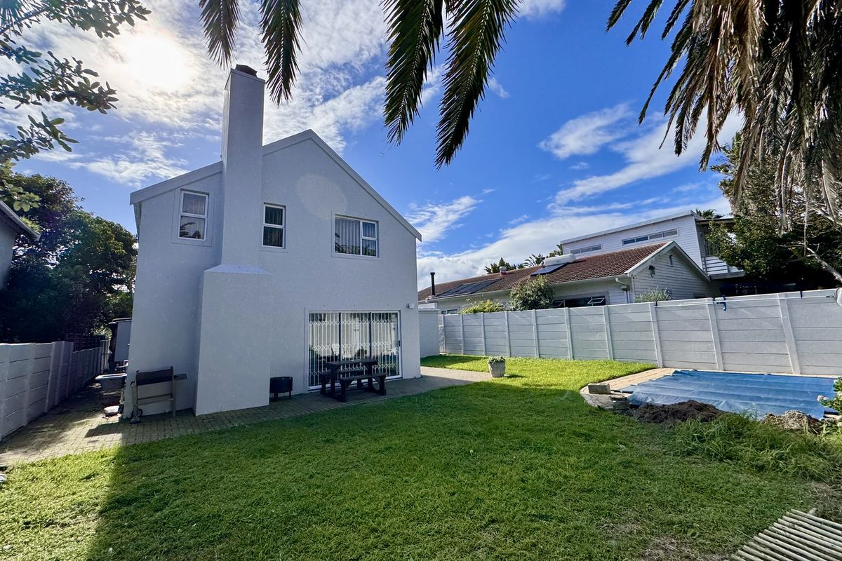 Rear view of the property featuring a paved patio, lawn, swimming pool with cover, and a white exterior finish with a prominent chimney.