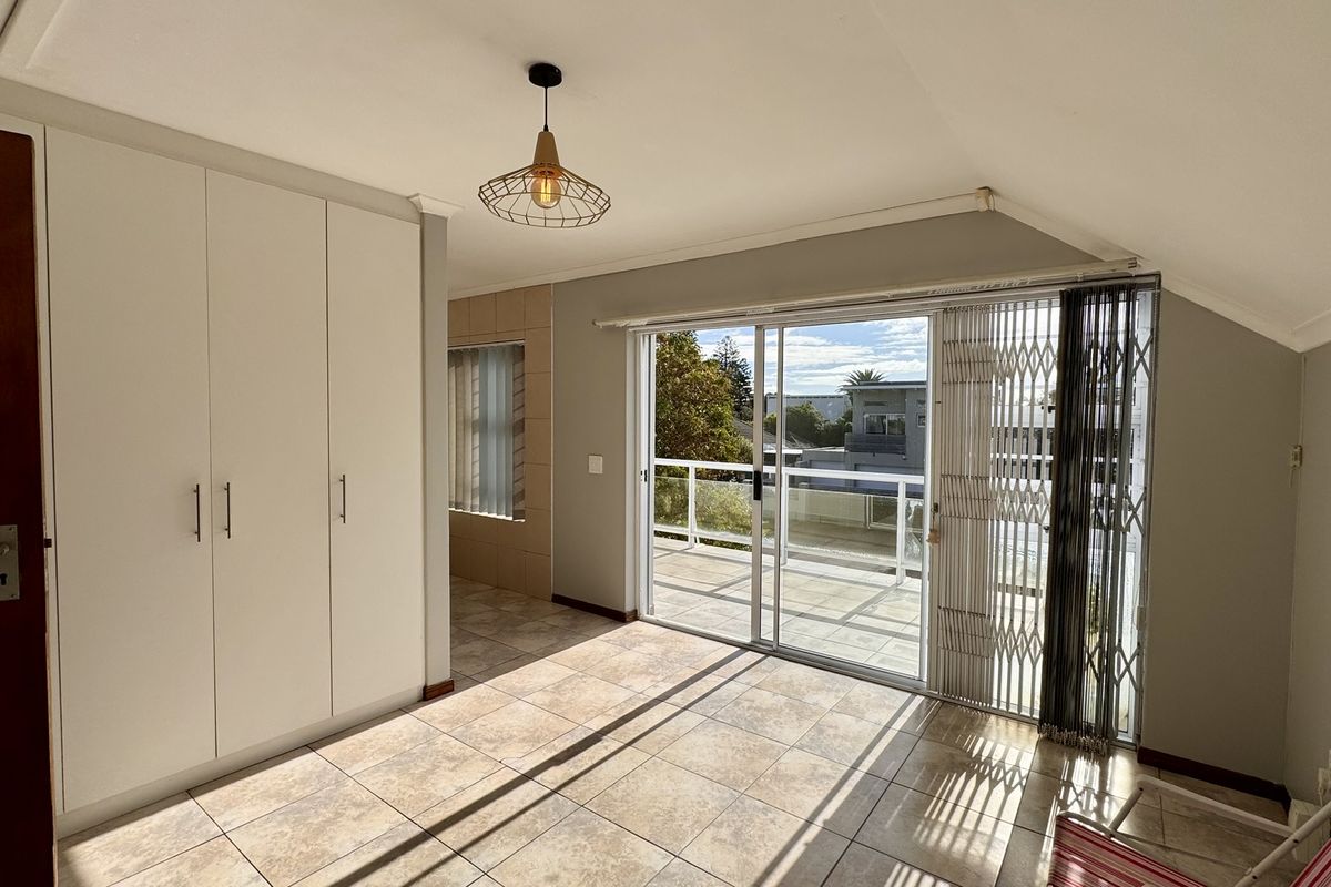 A bright, empty bedroom featuring built-in cupboards, tiled flooring, and sliding glass doors that open onto a private balcony.