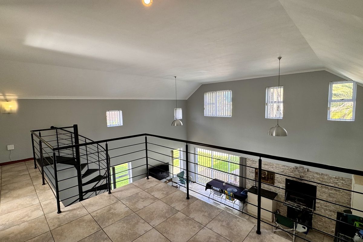 Spacious mezzanine living area featuring a modern spiral staircase, tiled flooring, vaulted ceilings, and an open view overlooking the ground floor living space.