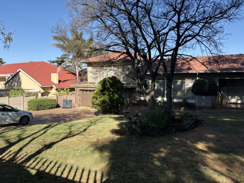 Front view of a residential property featuring a tiled roof, paved driveway, garage, and a balcony, set within a landscaped garden area.