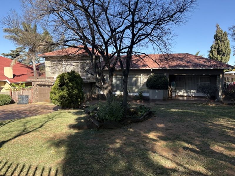 Front view of a residential house featuring a tiled roof, paved driveway, attached garage, and a spacious front garden with mature trees.