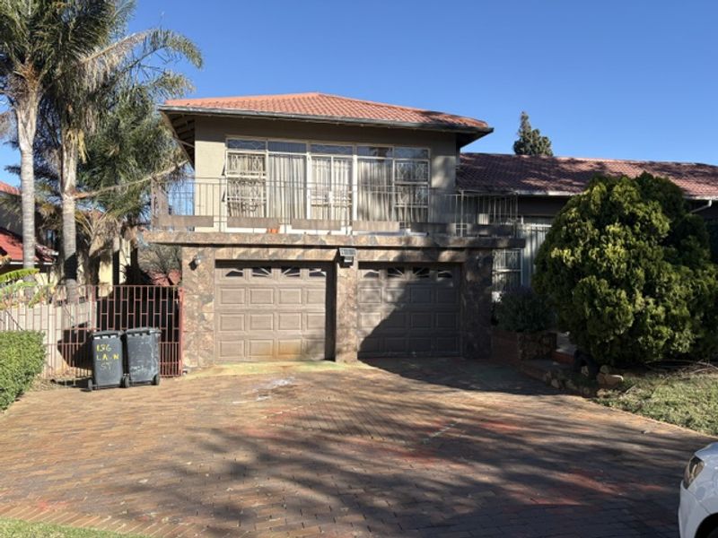 Front elevation of a double-story house featuring a double garage, paved driveway, and an upper-level balcony with stone cladding accents.