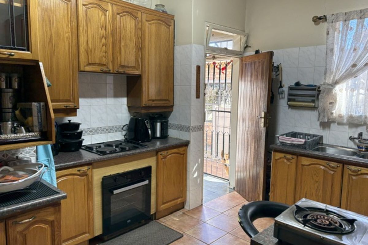A functional kitchen featuring traditional wooden cabinetry, built-in oven, electric hob, and direct access to an outdoor area through a timber door.