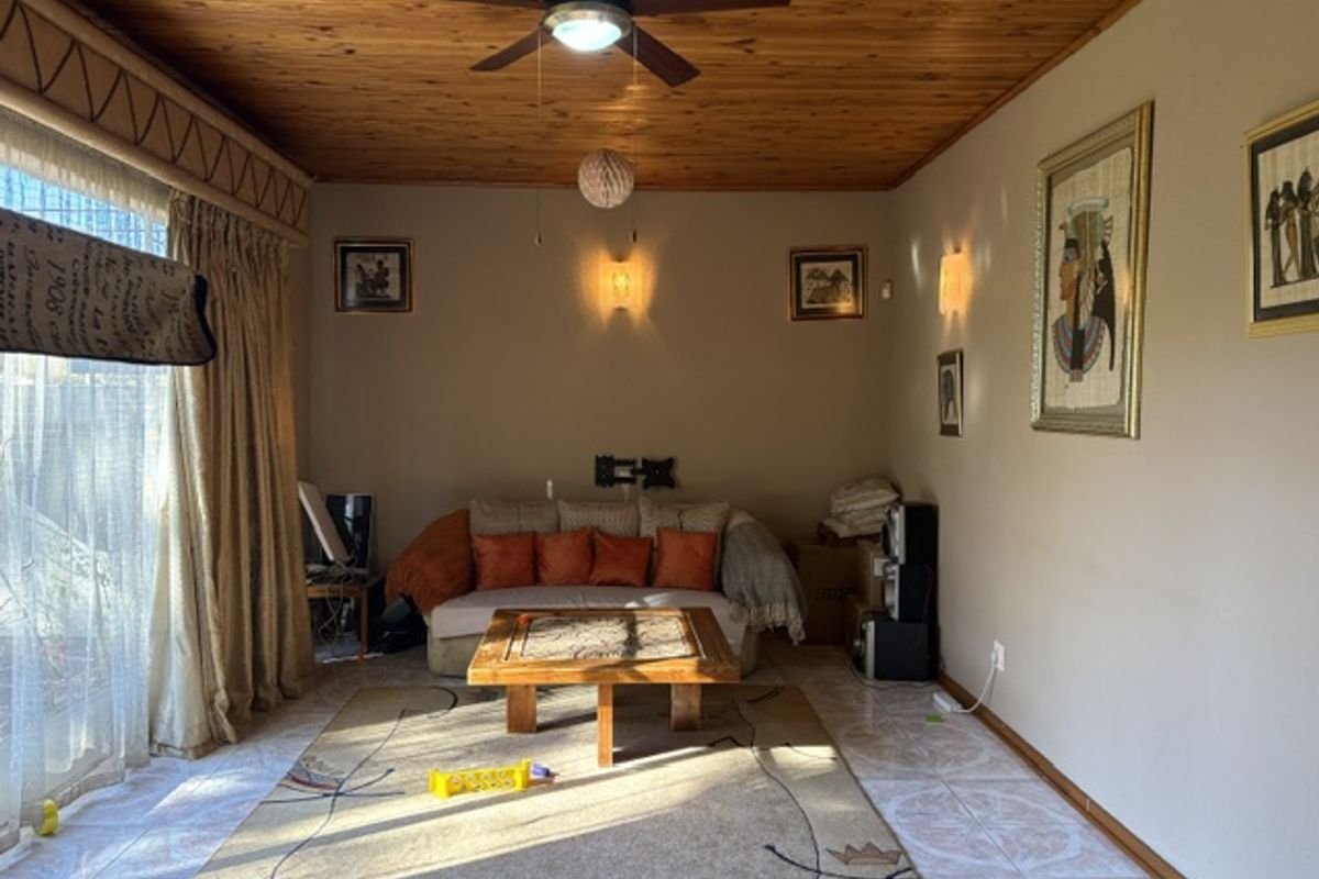 A living room featuring a timber ceiling, ceiling fan, and tiled flooring, illuminated by wall sconces.