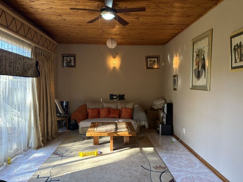 A living room featuring a timber ceiling, ceiling fan, and tiled flooring, illuminated by wall sconces.