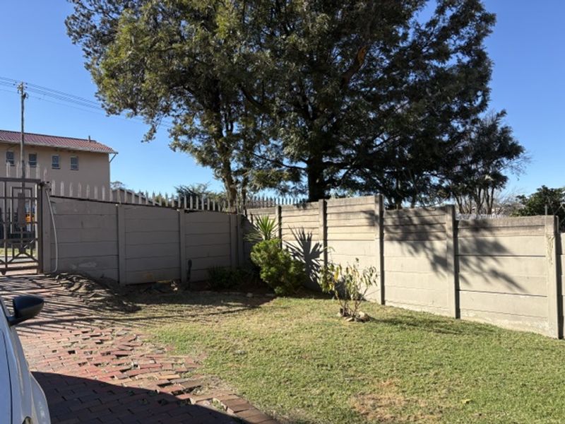 Front exterior view featuring a brick paved driveway, a precast concrete boundary wall with security spikes, and established trees.