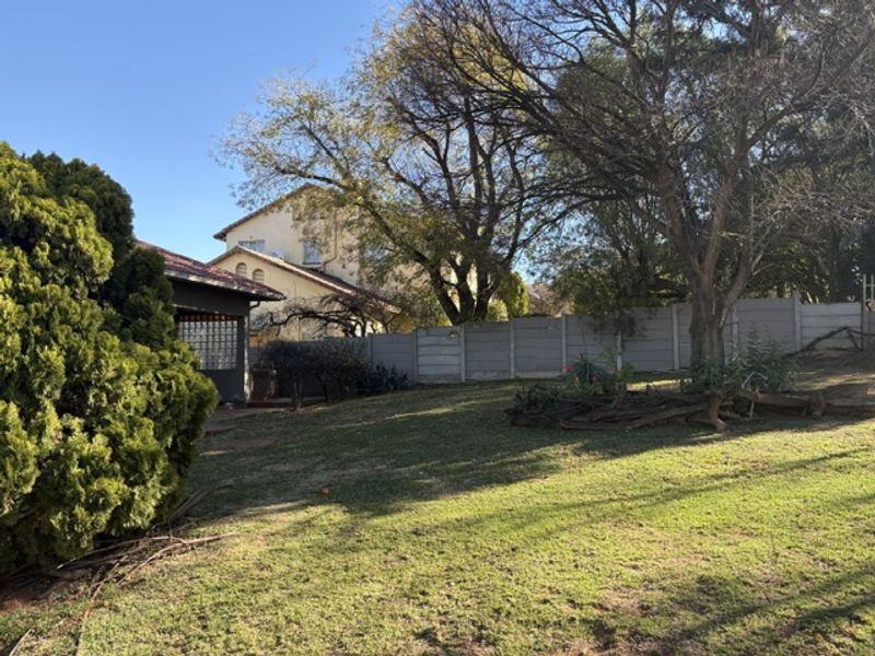 A spacious backyard garden featuring a large lawn, mature trees, and a precast concrete boundary wall.