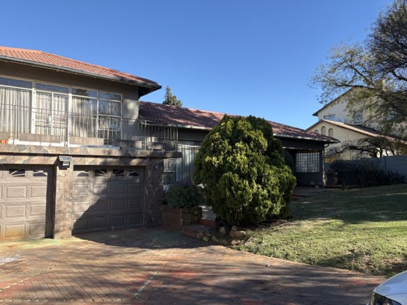 Front elevation of a residential property featuring a double garage, paved driveway, and an upper-level balcony with a tiled roof.