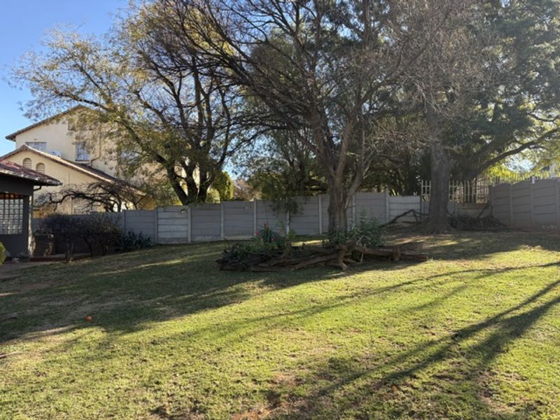 A spacious backyard garden featuring a well-maintained lawn, mature trees, and a secure precast concrete boundary wall.
