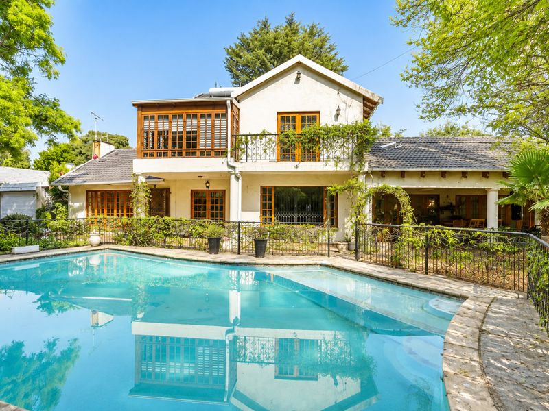 Rear view of the property featuring a swimming pool with stone coping, wrought iron fencing, and a two-story structure with a balcony.