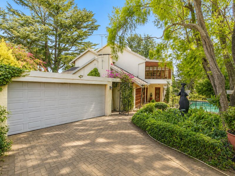 Front exterior view of the house featuring a paved driveway, double garage, landscaped garden, and a glimpse of the swimming pool area.