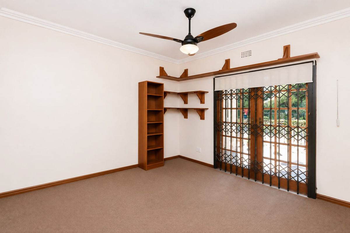 A bright, empty bedroom featuring neutral carpeting, a ceiling fan, built-in wooden shelving, and secure french doors leading to the exterior.