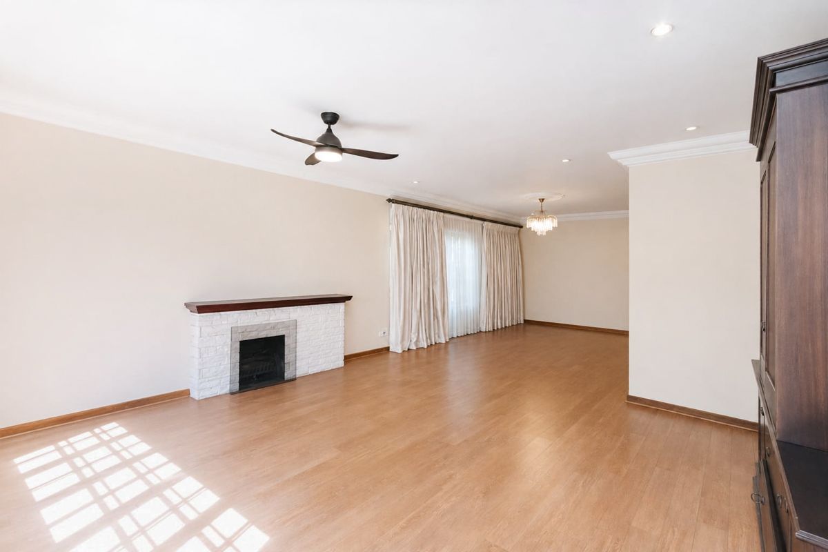 Spacious living room featuring laminate flooring, a white brick fireplace, crown molding, and elegant lighting fixtures.