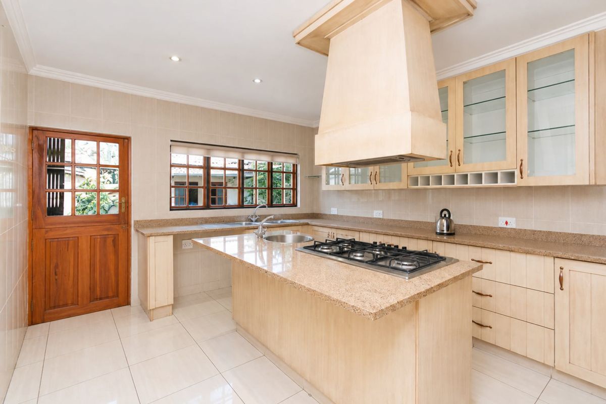 A well-maintained kitchen featuring light wood cabinetry, granite countertops, a central island with a gas hob, and tiled flooring.