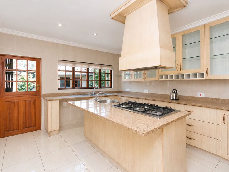 A well-maintained kitchen featuring light wood cabinetry, granite countertops, a central island with a gas hob, and tiled flooring.