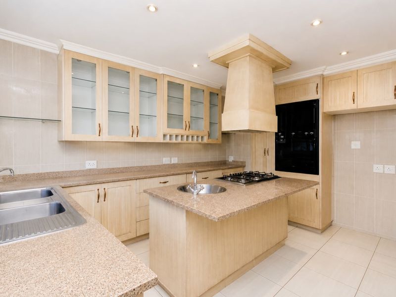 A spacious, well-maintained kitchen featuring light wood cabinetry, stone countertops, a central island with a gas hob, and integrated appliances.