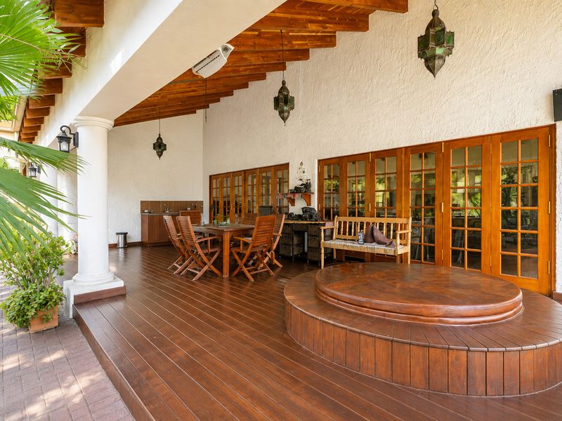 Spacious covered patio featuring timber decking, exposed wooden rafters, built-in cabinetry with sink, and a raised integrated hot tub.