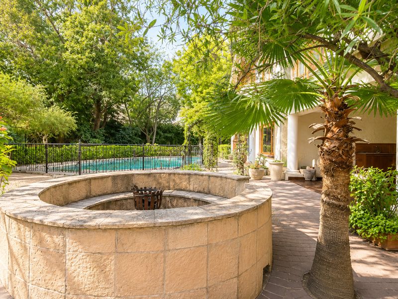 Outdoor entertainment area featuring a paved patio, a built-in stone fire pit, and a swimming pool enclosed by a wrought iron fence.