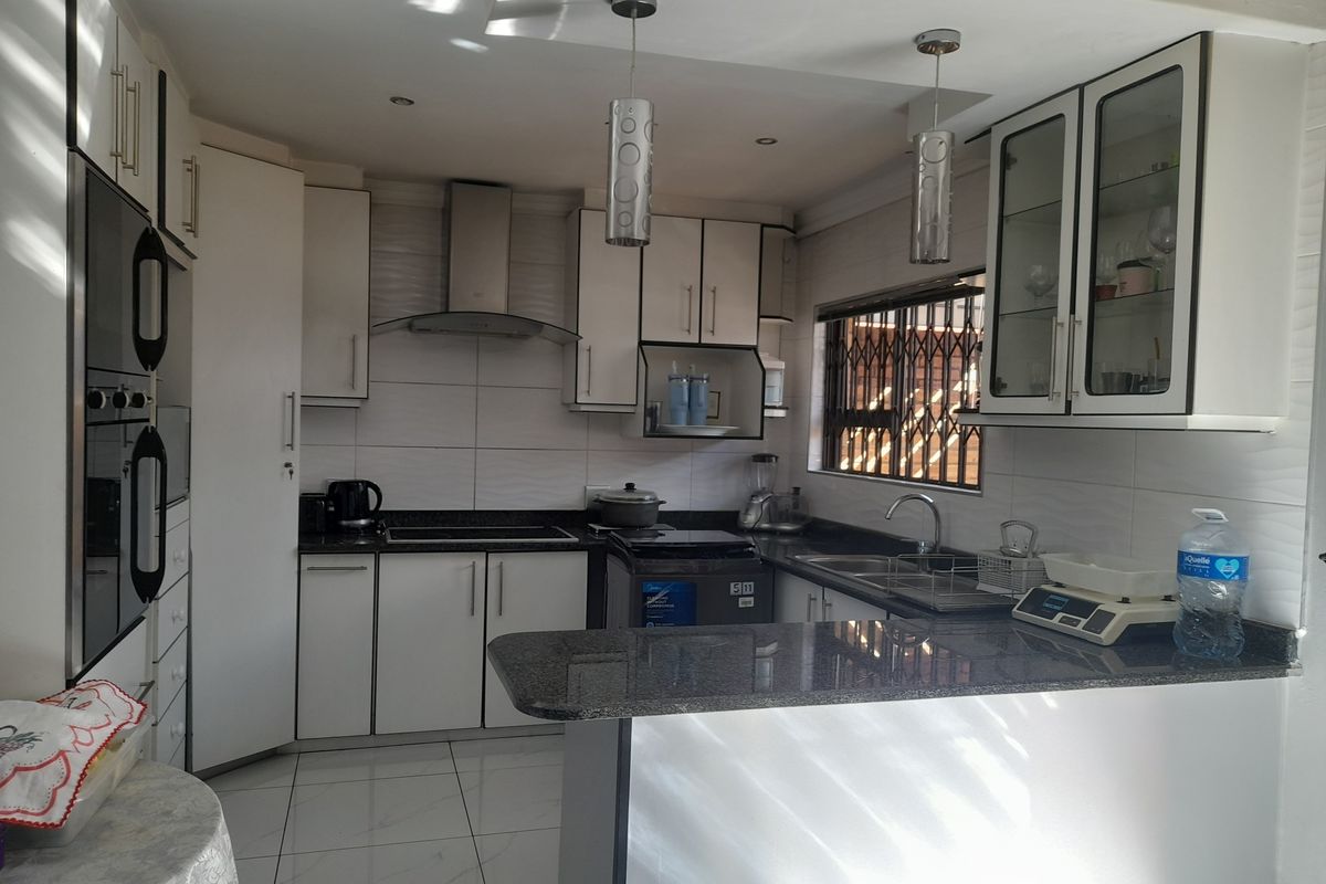 Modern kitchen featuring white cabinetry, granite countertops, a breakfast bar, built-in oven, and stainless steel extractor fan with tiled flooring.