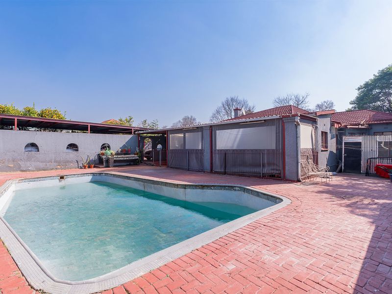 Outdoor pool area featuring a swimming pool, brick paved surround, and a covered patio area, offering potential for renovation and landscaping.